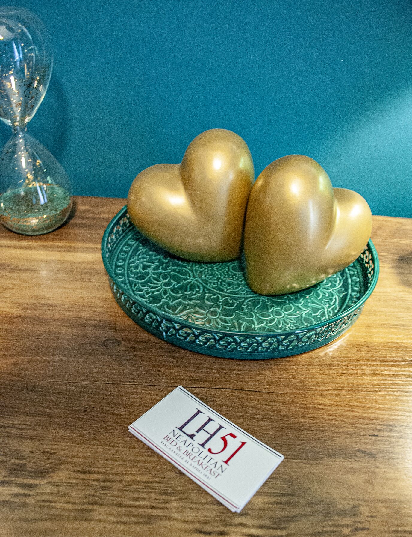 Een decoratief object met een hartvormig ontwerp op een groene schaal, geplaatst op een houten ondergrond voor een blauwe achtergrond.