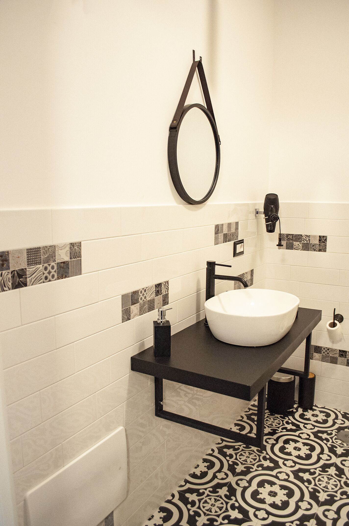 Une salle de bain moderne avec un plan de toilette noir, un lavabo blanc et des carreaux de sol à motifs.