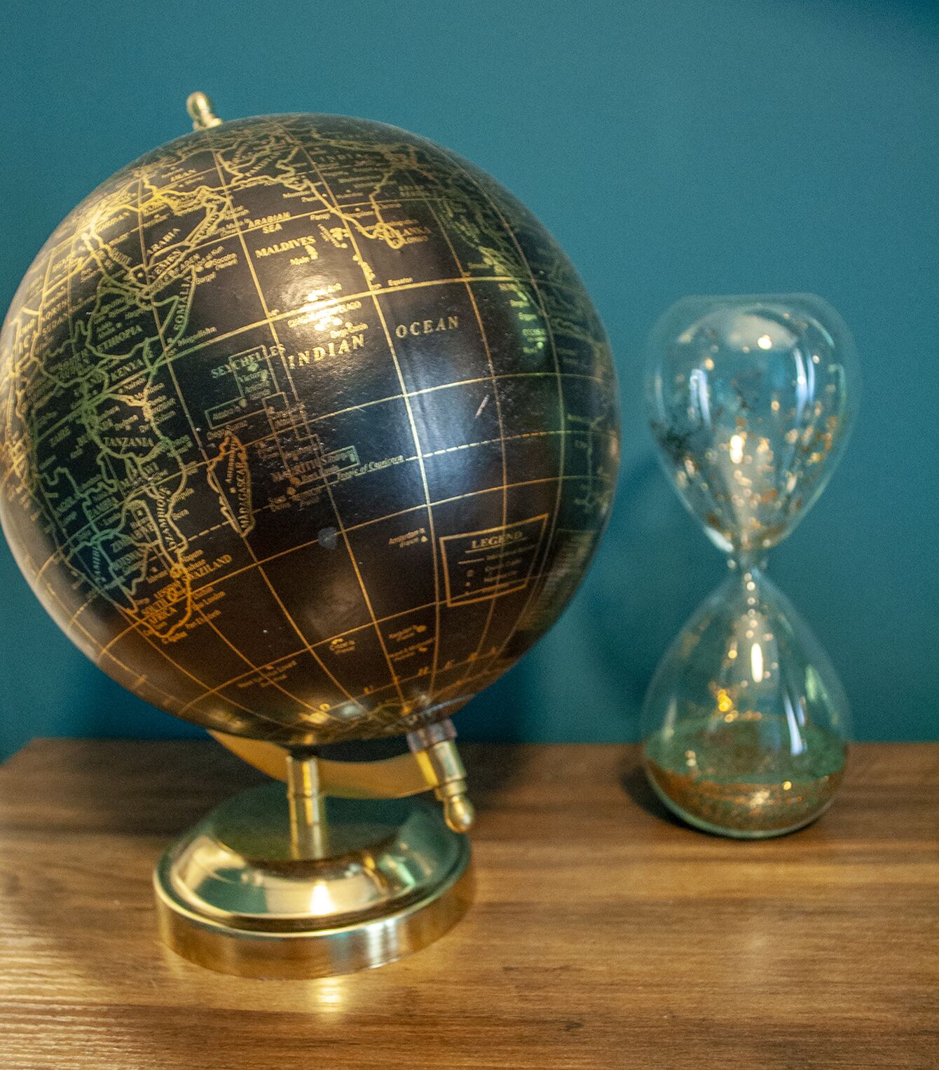 A globe with a stand and an hourglass on a wooden surface.