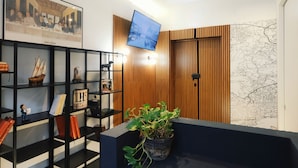 A modern room with a wooden panel wall, a mounted television, a map, and a bookshelf with various items. - LH 51 Neapolitan Rooms (Naples)