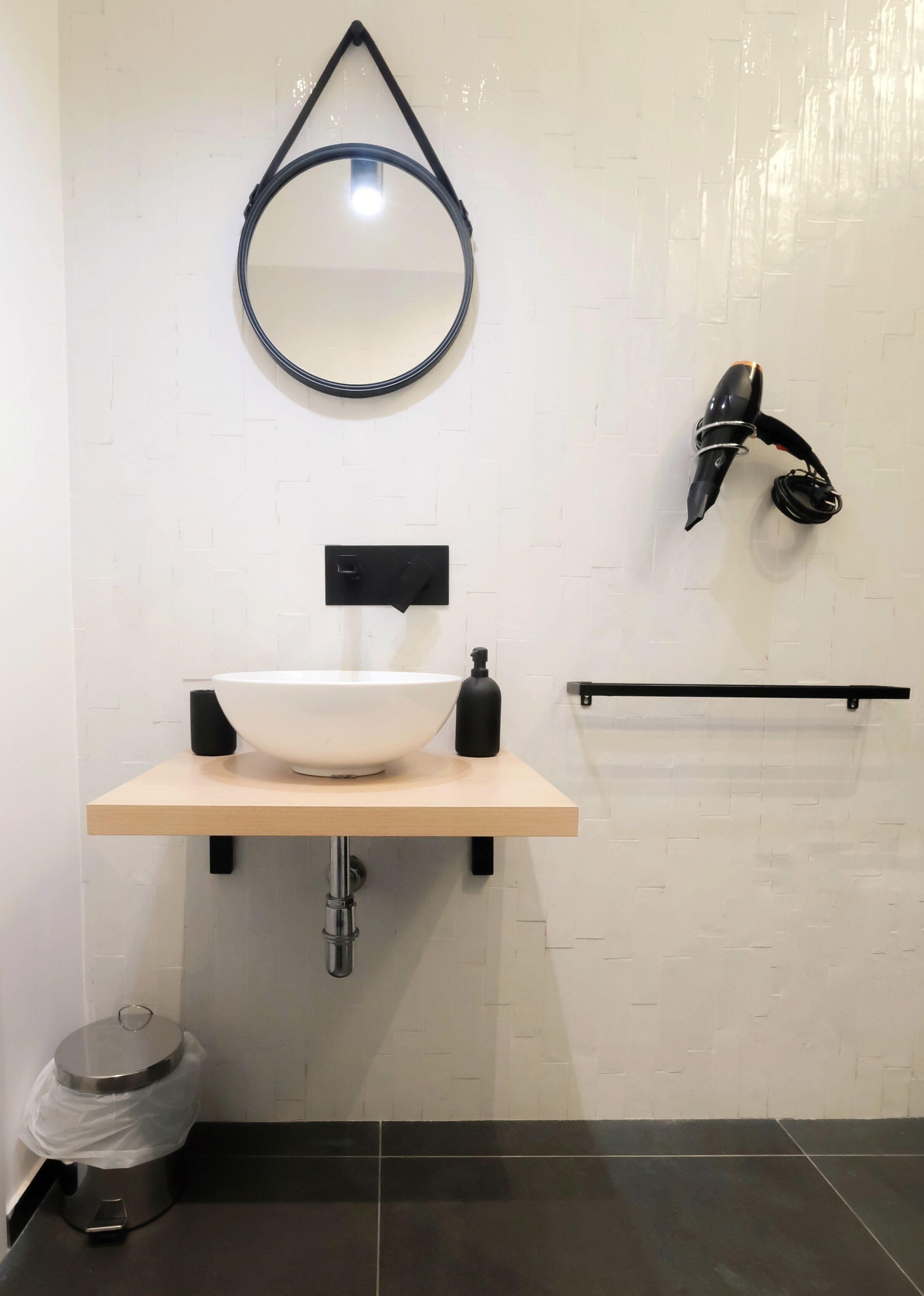 A modern bathroom with a white sink, black faucet, and a round mirror.