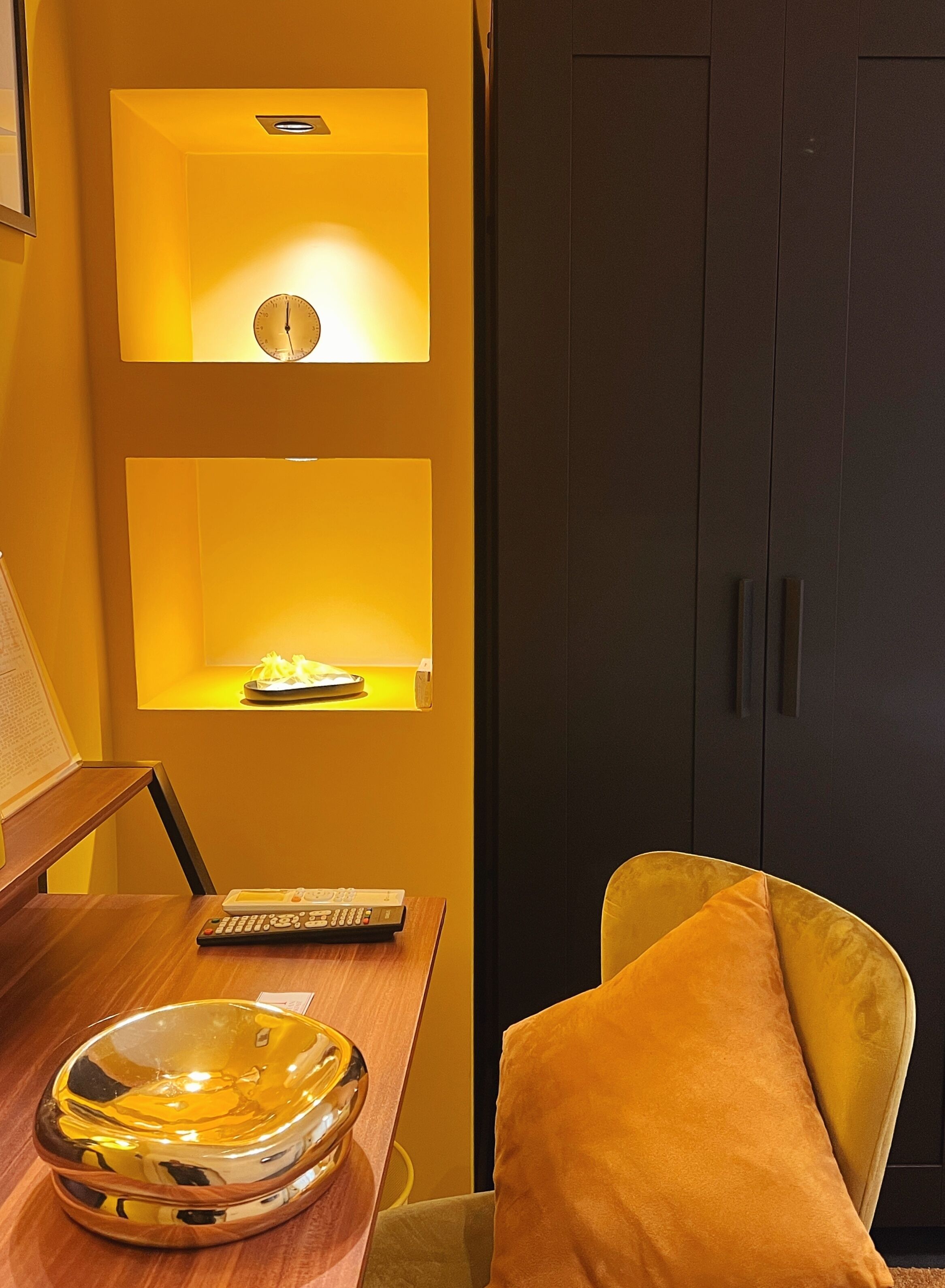 A room with a wooden desk, a bowl, a remote control, and a yellow chair.