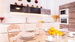 Una cocina moderna con armarios blancos, un estante superior negro y una pared de acento de madera. Hay dos hornos, un microondas y un frutero sobre la encimera.
