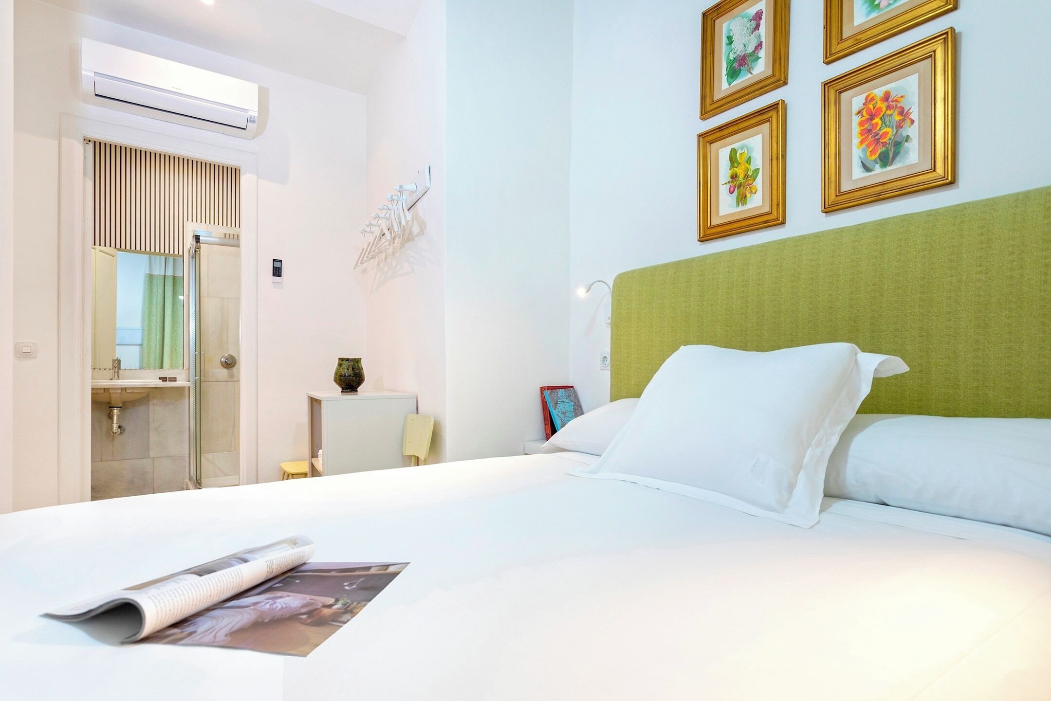 A hotel room with a bed, a bedside table, a mirror, and a wall with framed pictures.