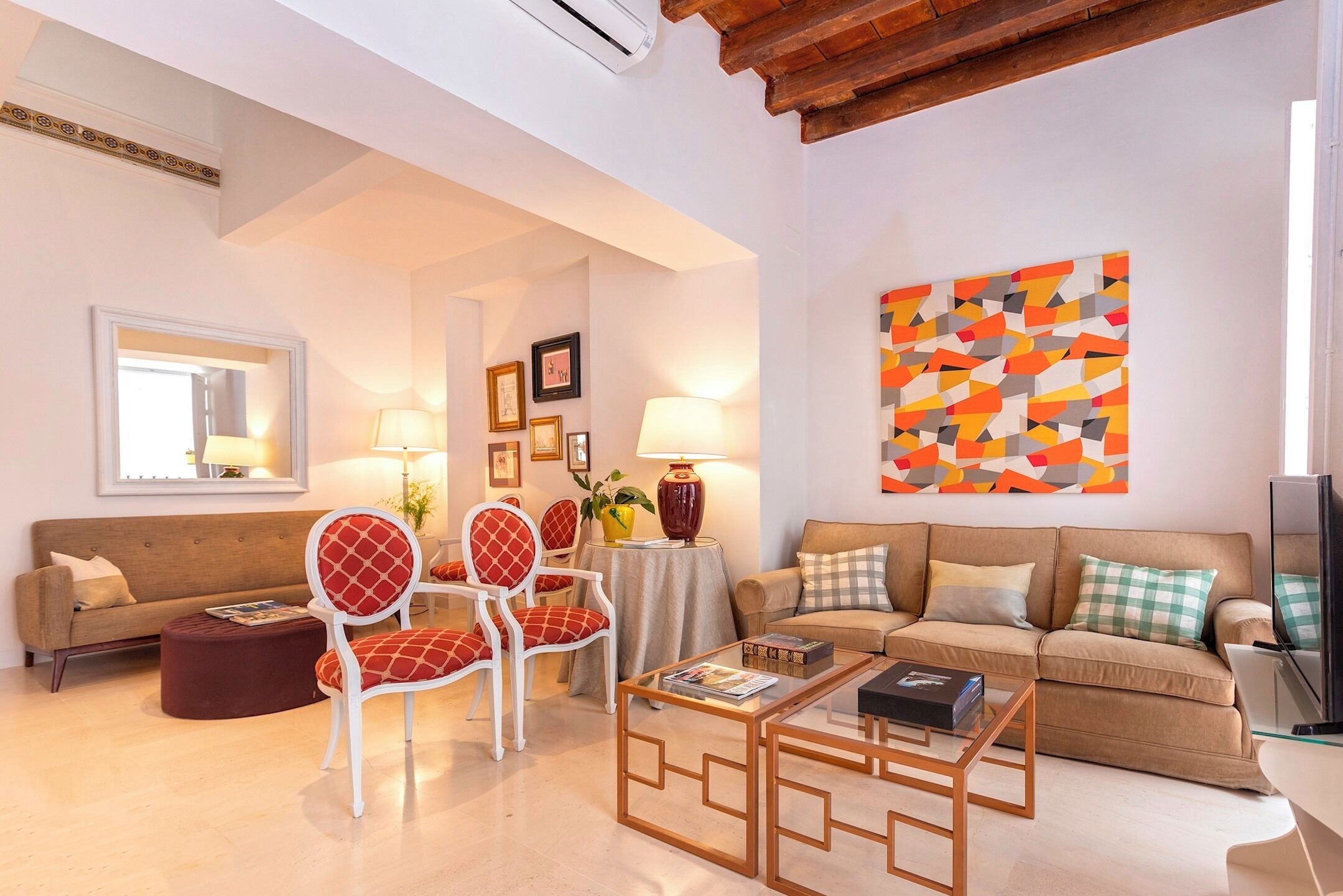 A living room with two sofas, a coffee table, and a red and white chair. There is a painting on the wall and a lamp on a side table.
