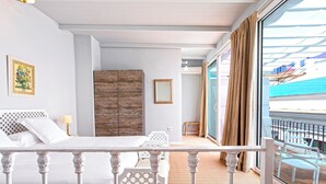 Un dormitorio con cama, armario de madera, una mesita y un balcón con vista al mar.
