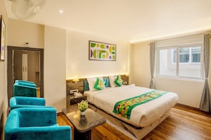 A hotel room with a bed, a desk with a lamp, a chair, a small table with a plant, and a window with curtains. - Treebo Golden Leaf (Ranchi)