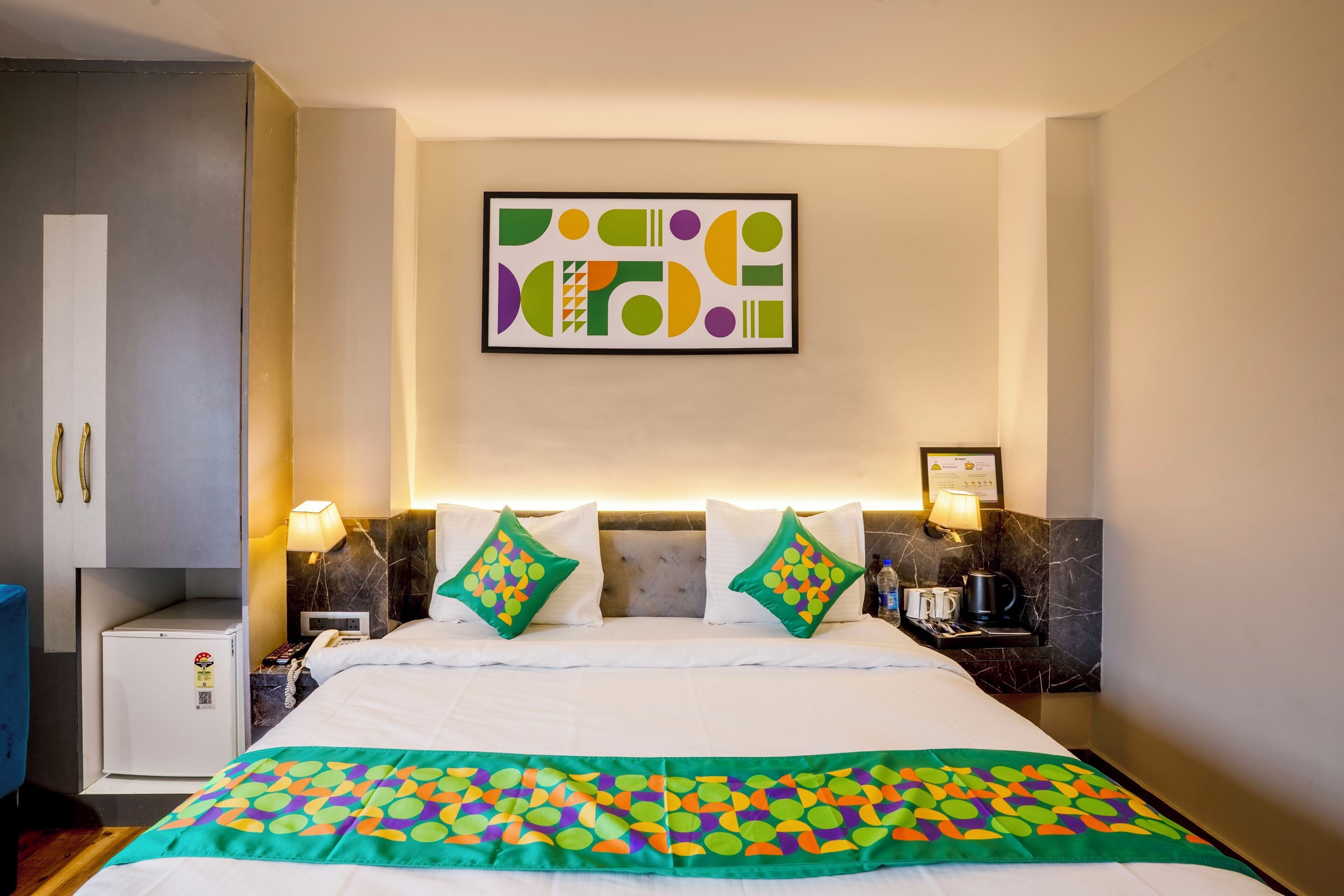 Ein Hotelzimmer mit Bett, kleinem Schreibtisch, Nachttisch, Wandbild und Wandlampe.