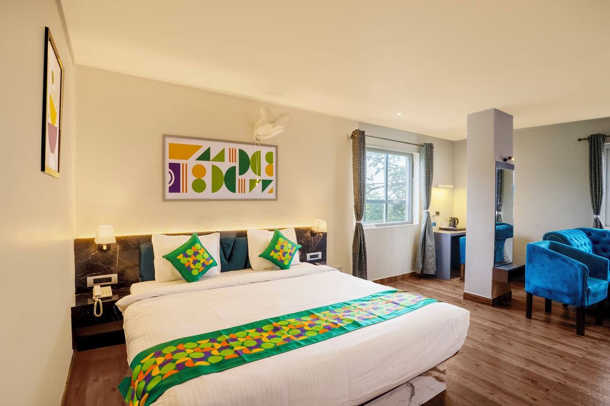 A hotel room with a large bed, a desk, a chair, and a window with curtains.