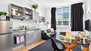 A modern kitchen with a dining area, a sofa, and a large window with curtains. - Stay in Aucklands Iconic Queen St  Zodiak Stays (Auckland)