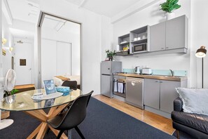 A compact kitchen with a microwave, oven, and a small refrigerator. There is a dining table with chairs and a glass-top table.