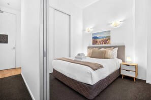 A hotel room with a bed, a nightstand, a wall-mounted lamp, and a painting.