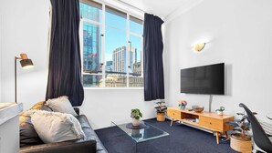 A modern living room with a sofa, a coffee table, a TV, and a city view through large windows. - Stay in Aucklands Iconic Queen St  Zodiak Stays (Auckland)