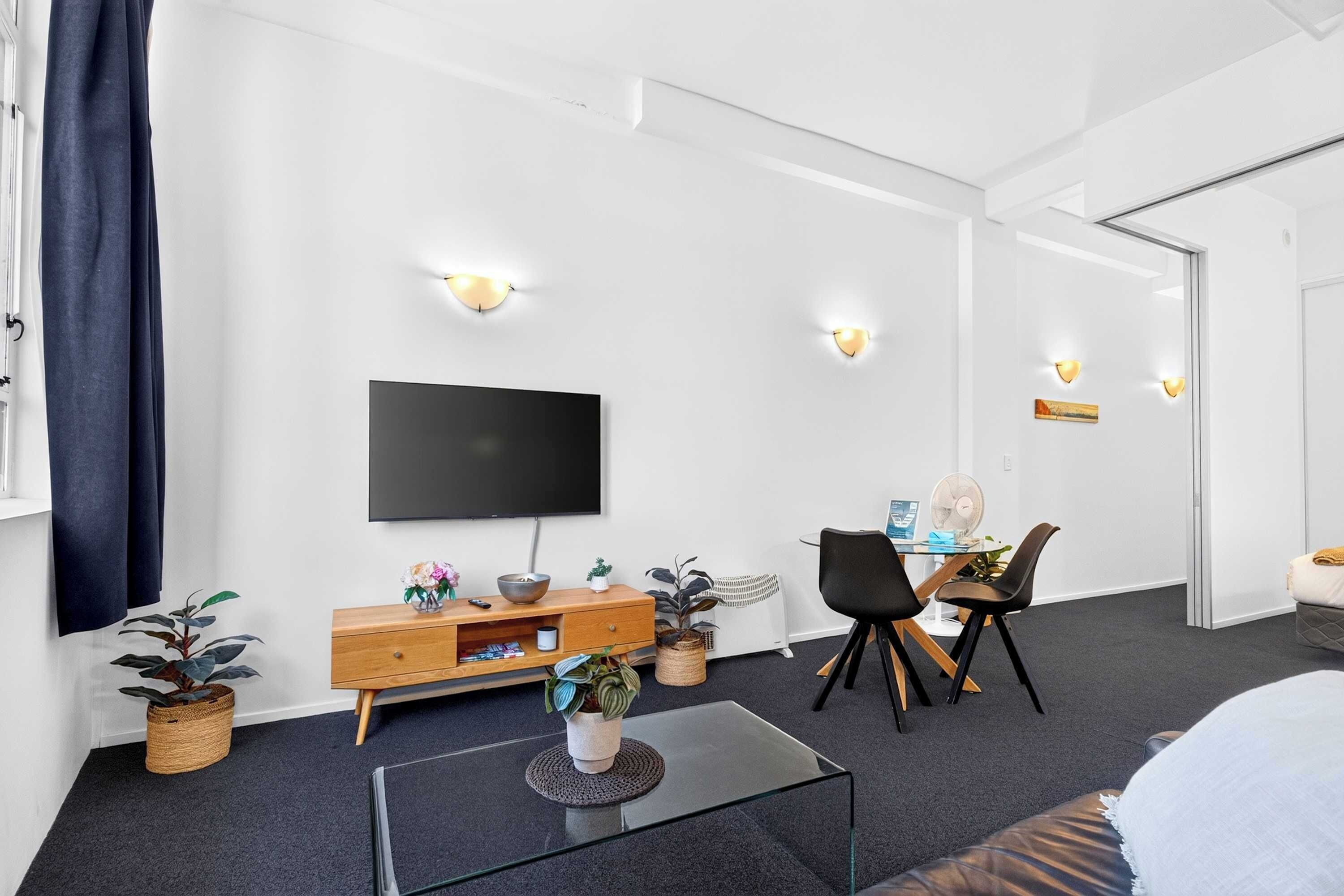 Ein modernes Wohnzimmer mit Flachbildfernseher, einem Holzkonsolentisch, einem Glastisch und einem Essbereich mit Stühlen und Tisch.