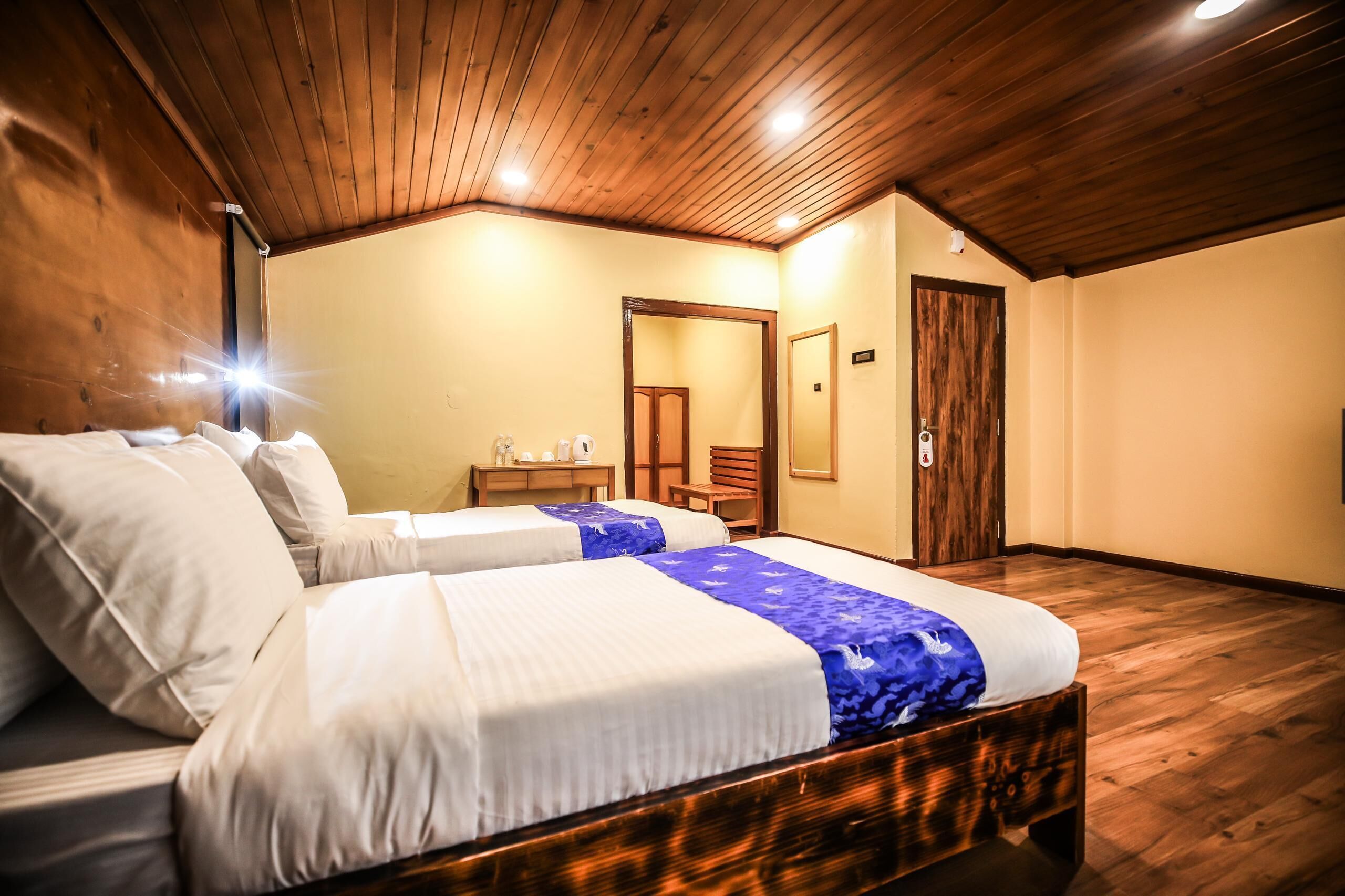 A bedroom with two beds, wooden ceiling, a small table with a mirror, and a door.
