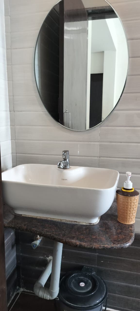 A bathroom with a white sink, a round mirror, and a small wicker basket.