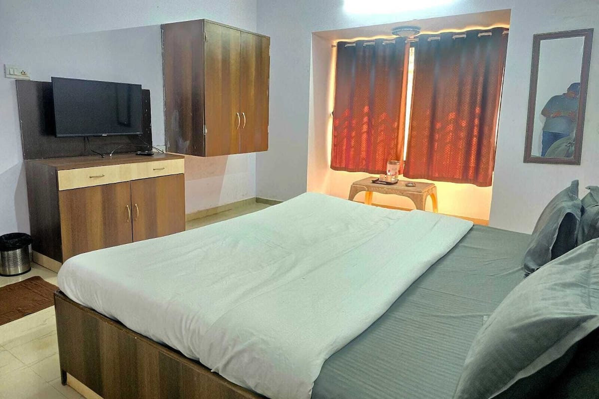 A bedroom with a bed, a TV, a wardrobe, and a window with curtains.