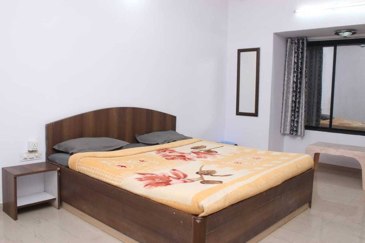 A bedroom with a wooden bed, a bedside table, a bench, and a window with curtains.