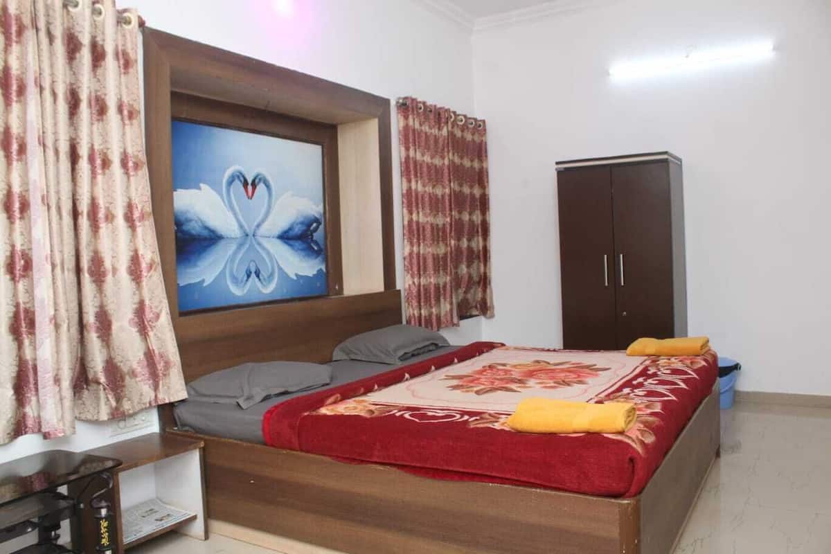 A bedroom with a wooden bed, a red and white patterned bedspread, grey pillows, a wooden headboard, a painting of swans, and a wardrobe.