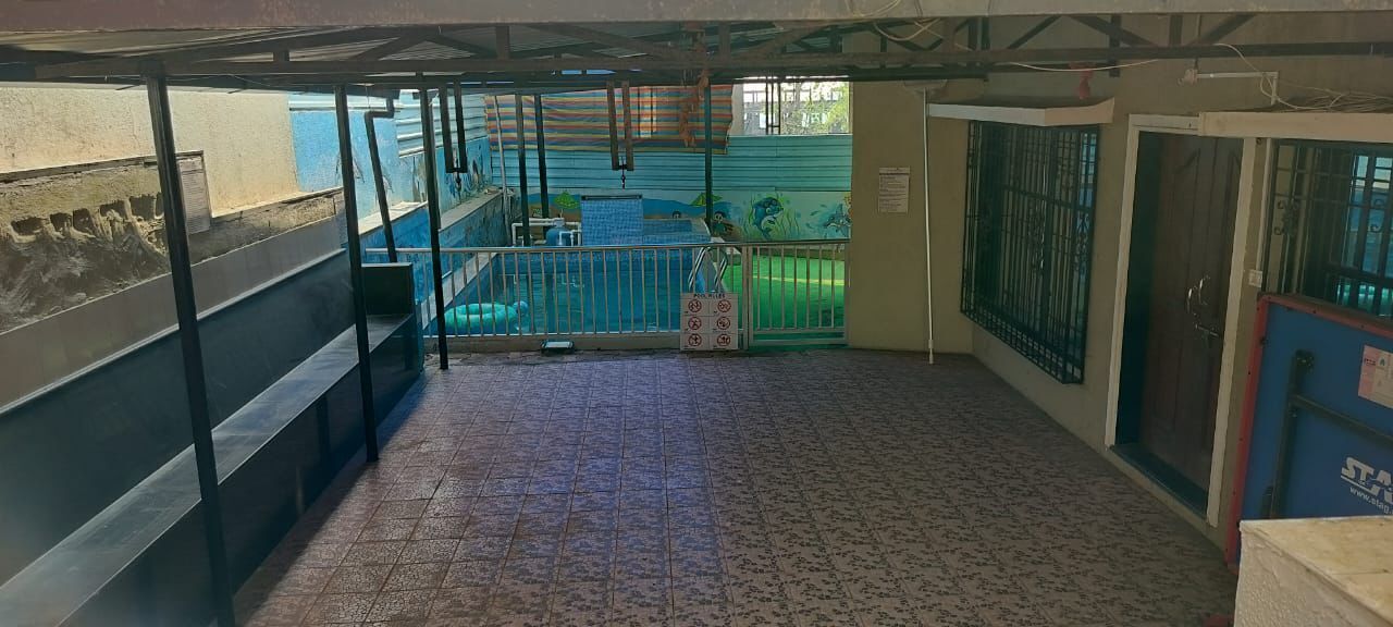 Un espacio exterior cubierto con suelo de baldosas, barandilla metálica y vista a una piscina.