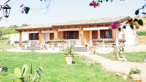 A house with a tiled roof, a front porch with potted plants, and a well-maintained lawn.