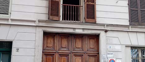A building with a large wooden double door, a balcony with metal railings, and a sign indicating a no parking zone.