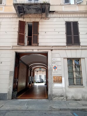 Une entrée d’immeuble avec une porte en arc de cercle, un panneau indiquant un parking, et un panneau interdisant le stationnement.