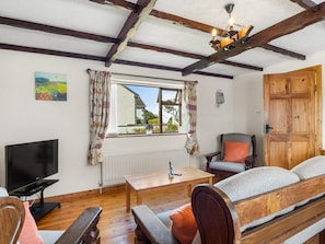 A cozy room with a wooden floor, a television, a wooden table, a sofa, and a chair.