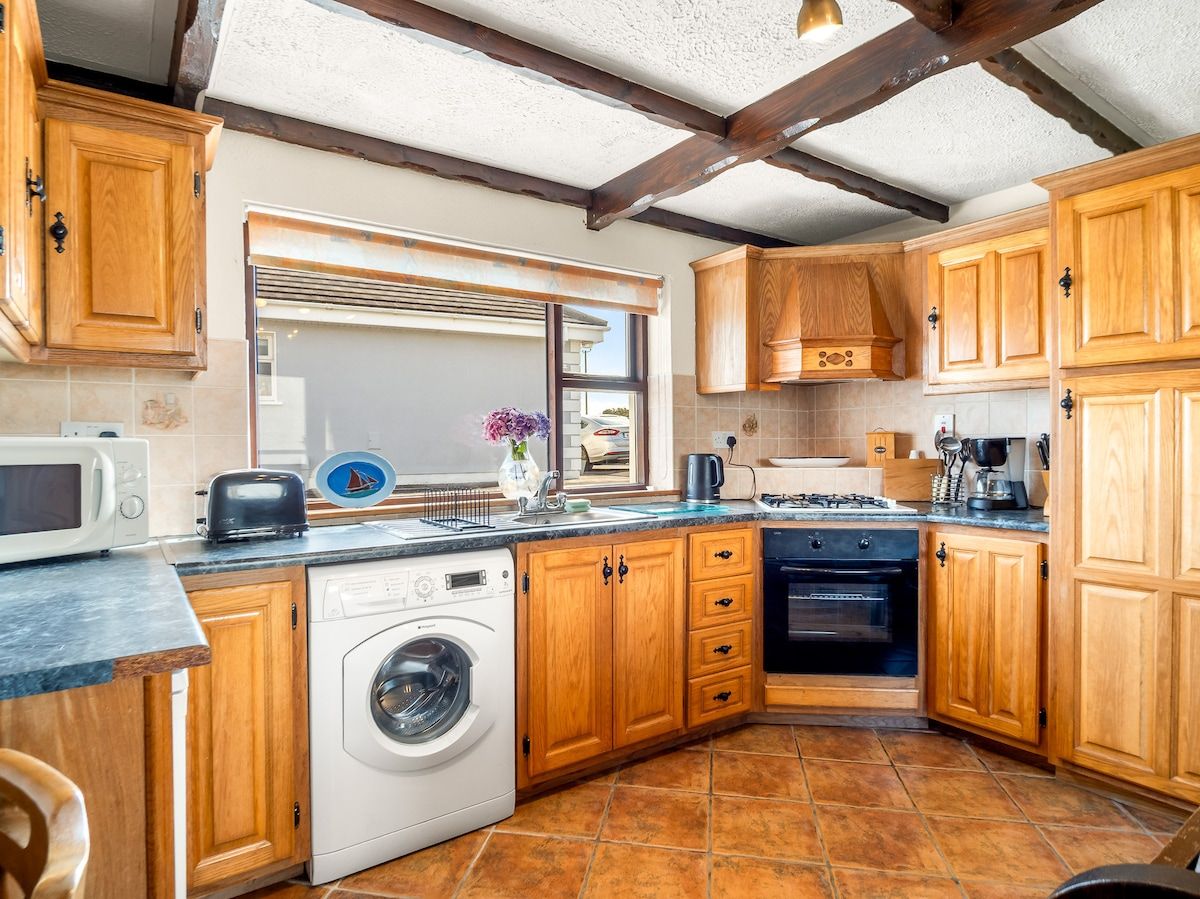 Een functionele keuken met houten kastjes, een wasmachine, een fornuis en een magnetron.