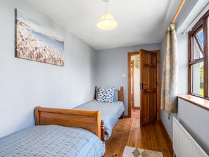 A bedroom with two wooden beds, a painting on the wall, a wooden door, and a window with curtains.