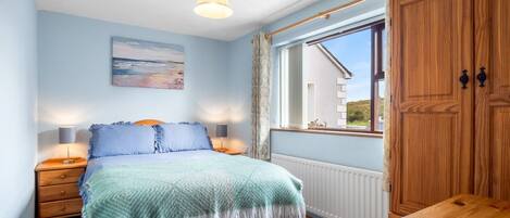 A bedroom with a bed, bedside lamps, a window with curtains, a wooden table, and a painting on the wall.