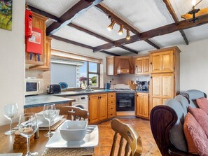 A kitchen with wooden cabinets, a dining table set with glasses and plates, and a sofa in the living area.