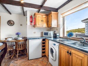 A compact kitchen with wooden cabinets, a washing machine, a microwave, and a dining area with chairs and a table.
