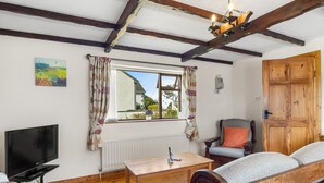A cozy room with a wooden ceiling, a television, a wooden table, a sofa, and a window with curtains.