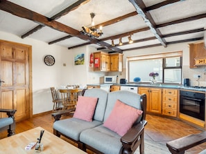 A cozy living room with a sofa and wooden furniture, a dining area with chairs, and a kitchen with wooden cabinets and appliances.