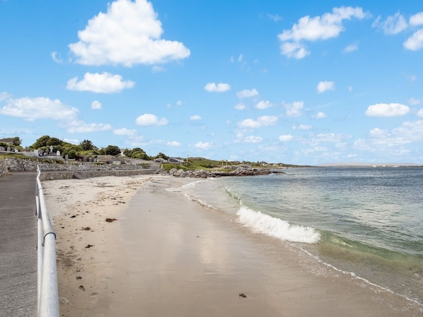 A beach with a paved walkway, clear skies, and calm water.