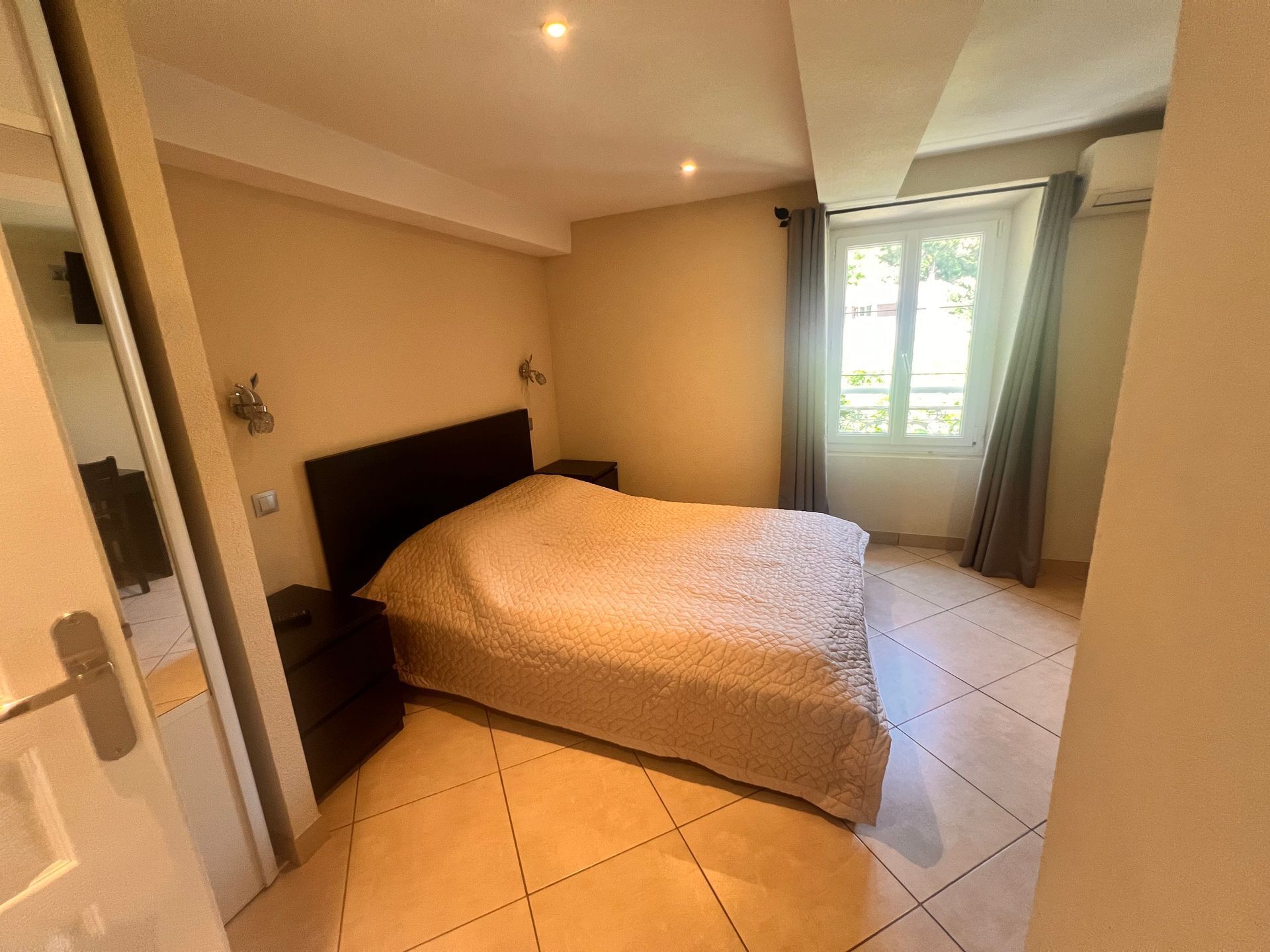A bedroom with a bed, a nightstand, and a window with curtains.