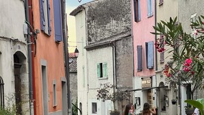 A narrow street with buildings on either side, a woman and a child walking, and potted plants along the sidewalk. - Résidence Callas (Callas)