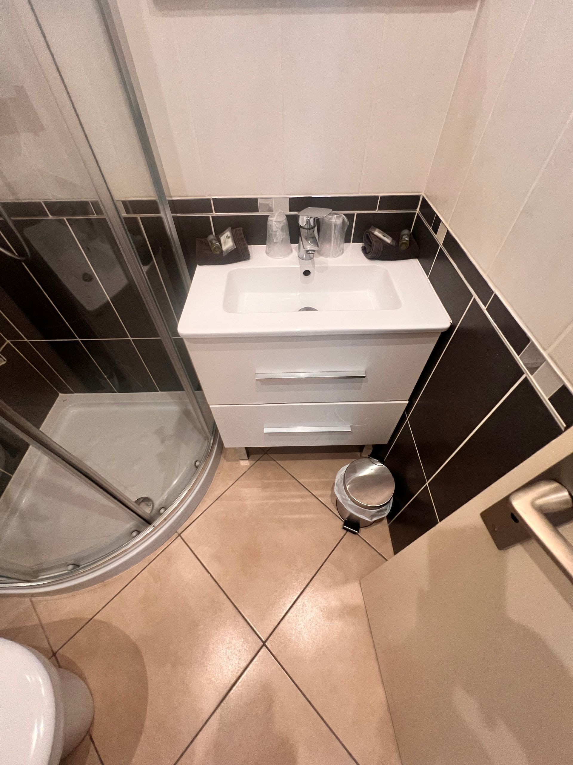 Ein Badezimmer mit einem weißen Waschbecken, Wänden mit Schwarz-Weiß-Fliesen, einer Duschkabine aus Glas und einer Toilette.