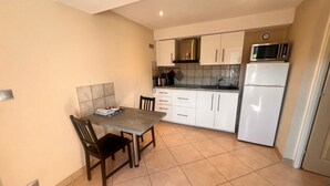A compact kitchen with white cabinets, a microwave, and a refrigerator. There is a dining table with chairs. - Résidence Callas (Callas)