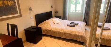 Un dormitorio con dos camas, un escritorio, una silla, un cesto de basura y una ventana con cortinas.