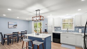 Una cocina moderna con armarios blancos, una isla azul y una zona de comedor con sillas de madera.