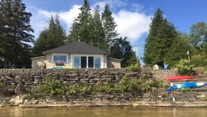 Un muro de piedra con una casa al fondo, un cuerpo de agua cristalina en primer plano y kayaks a la derecha.