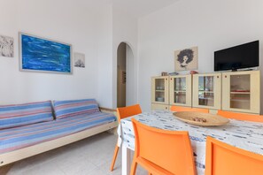 A room with a bed, a dining table with chairs, a television, and a cabinet with glass doors.
