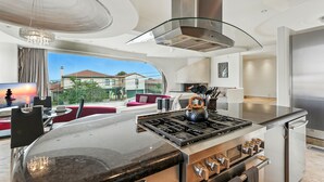 A modern kitchen with a central island, stainless steel appliances, and a glass railing. - The Wave House | Custom Gem w/ Panoramic Views, Fire Pit, BBQ, Pool Table & Wraparound Balconies (San Diego)