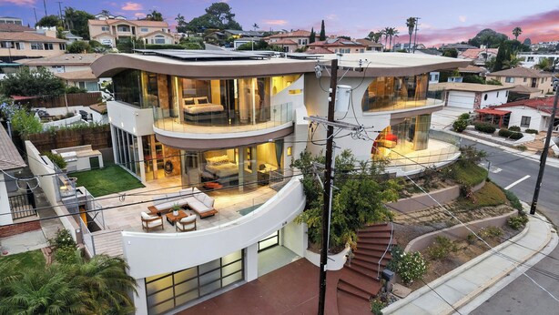 A modern multi-story house with a curved design, large glass windows, and a rooftop patio. - The Wave House | Custom Gem w/ Panoramic Views, Fire Pit, BBQ, Pool Table & Wraparound Balconies (San Diego)