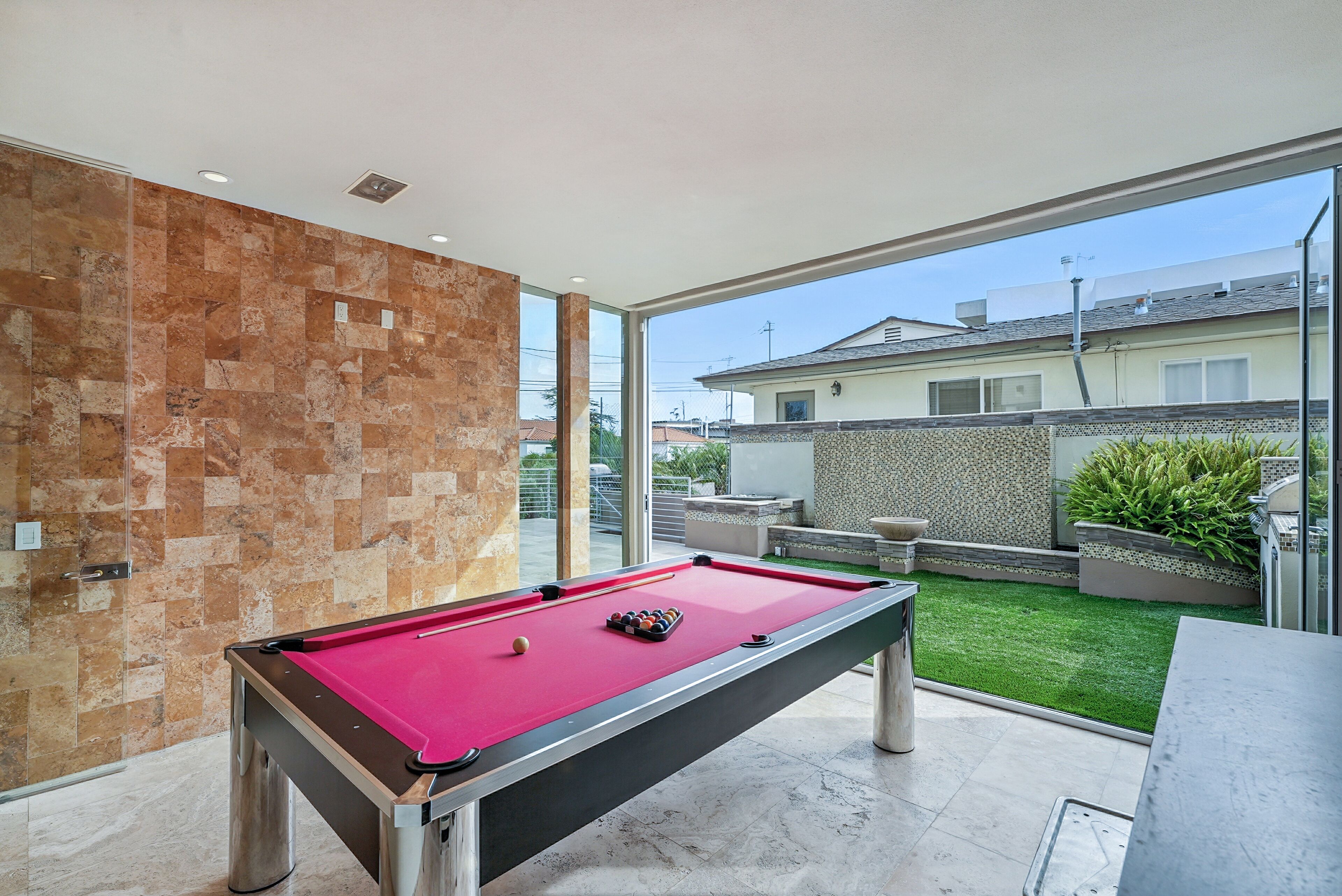 A pool table in a modern room with a stone wall and a view of a residential area.