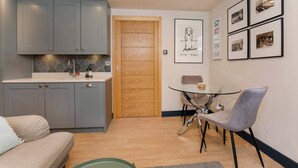A compact kitchen with grey cabinets, a wooden door, and a dining area with a glass table and grey chairs.
