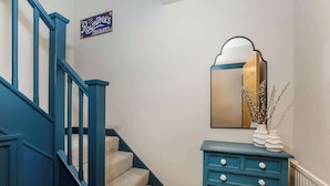 Una scala con ringhiere blu e gradini ricoperti di moquette beige, un mobile vanitario blu con cassetti e un cartello sopra le scale che indica   “Roundtree’s Chocolates”.