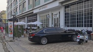 Een zwarte auto geparkeerd voor een gebouw met een bord waarop 'BAH COFFEE' staat.